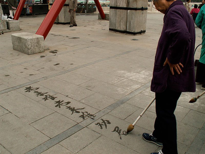 Un homme pratique sa calligraphie au sol, simplement avec de l’eau. Passe-temps bon marché.